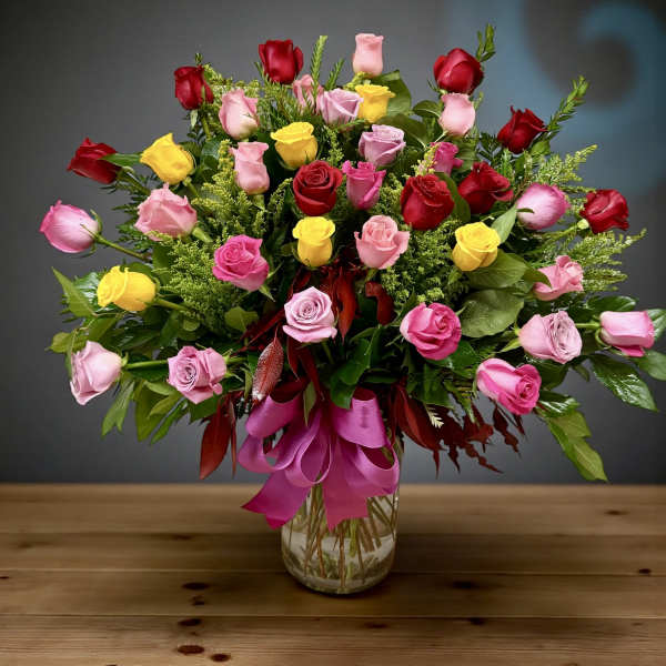 Mixed roses in pink, red, and yellow arranged in a glass vase with a ribbon.