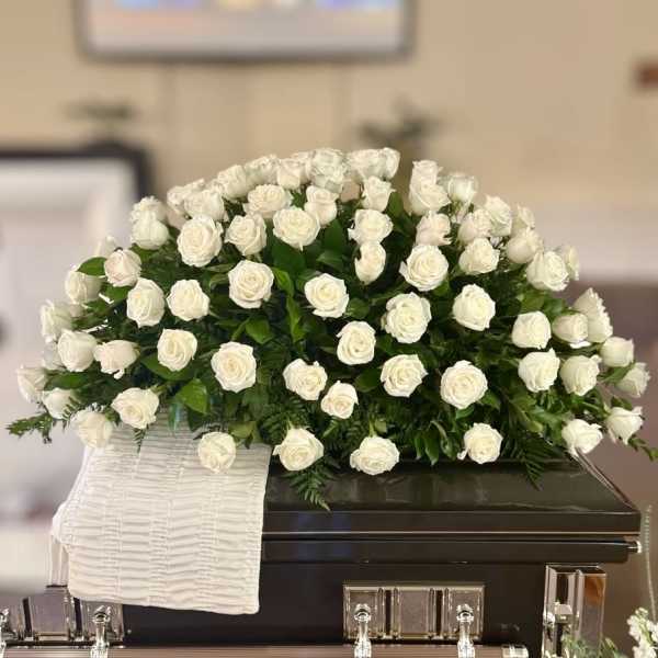 White rose casket spray on a dark casket with a white cloth drape