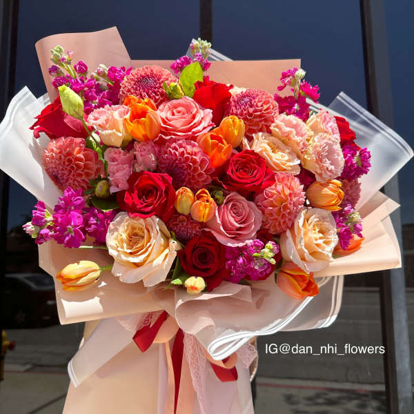 Large bouquet of red, pink, and peach flowers wrapped in blush paper