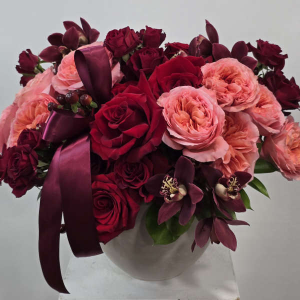 Bouquet of red and pink roses in a white vase with a burgundy ribbon