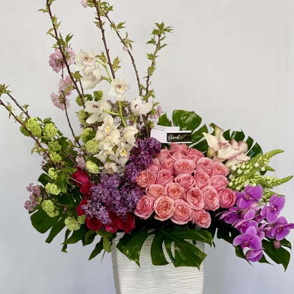 Large mixed floral arrangement in a white vase with pink, purple, and white blooms