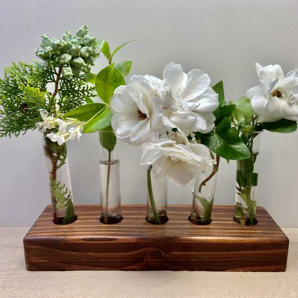 White flowers and greenery arranged in small glass tubes on a wooden base.