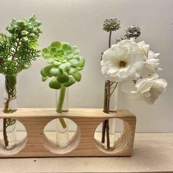 Three small floral stems in glass tubes on a wooden holder