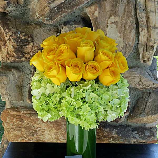 Yellow roses arranged with pale green hydrangeas in a tall green vase