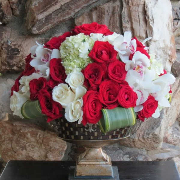 Red and white rose arrangement with white orchids in a decorative pedestal vase