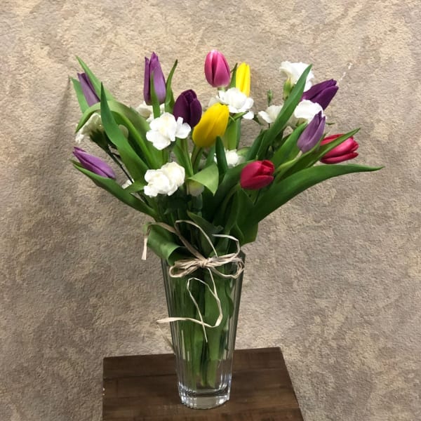 Colorful tulips and white carnations in a clear glass vase