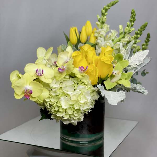 Yellow orchids, roses, and hydrangea in a black vase