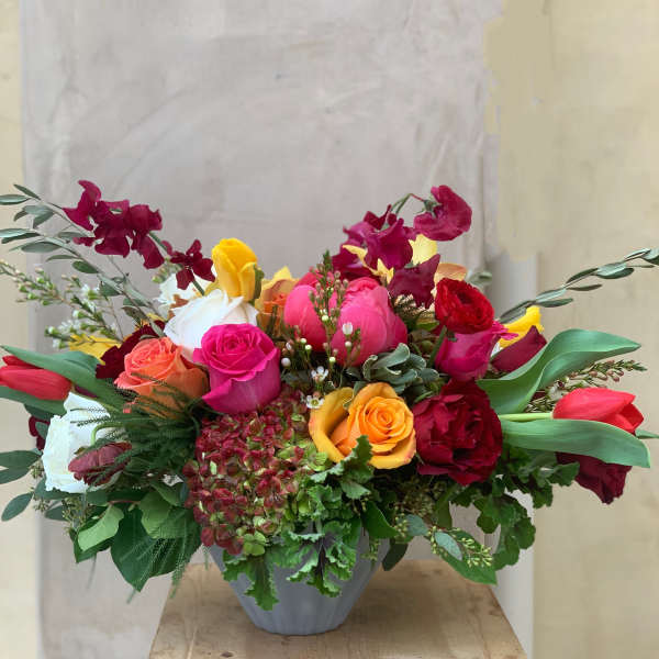 Mixed bouquet of roses, tulips, and orchids in a gray vase