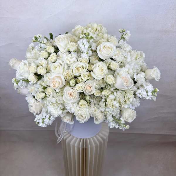 Large all-white bouquet of roses and hydrangeas in a white hatbox vase on a pedestal