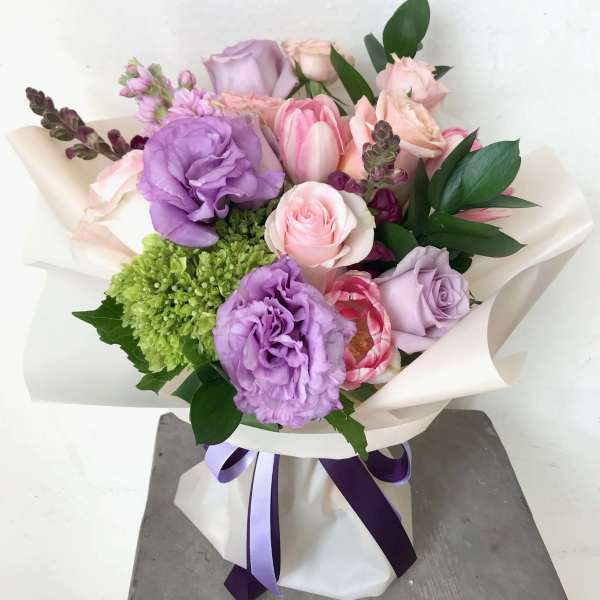 Bouquet of pink and lavender flowers wrapped in white paper with a purple ribbon