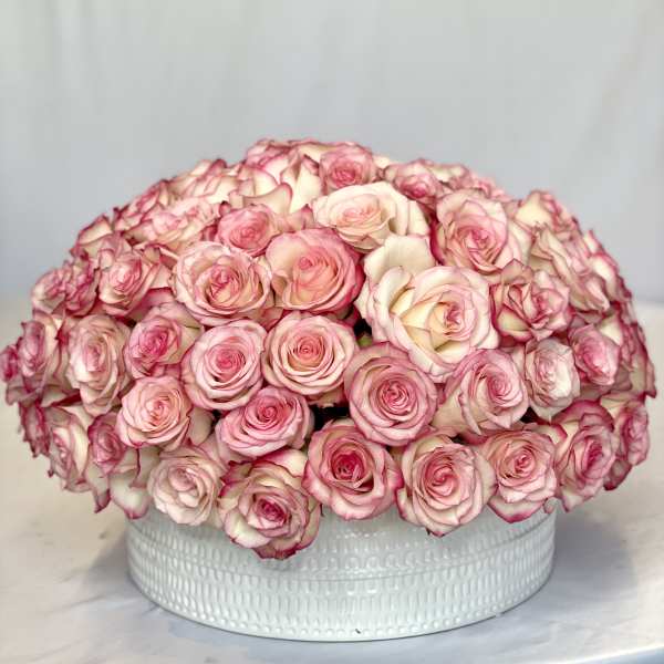 Round bouquet of pink and white roses in a white container