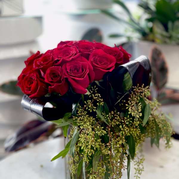 Red roses arranged in a clear glass vase with trailing greenery