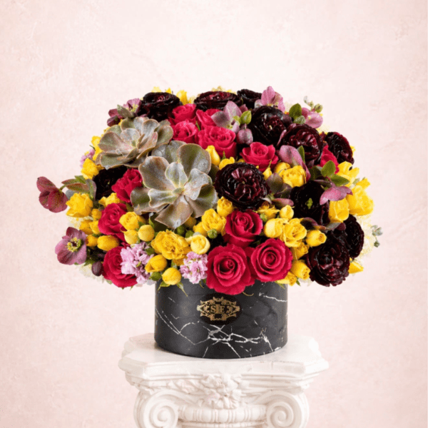 Mixed bouquet of pink, yellow, and dark red flowers in a black vase