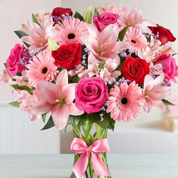 Pink and red bouquet of roses, lilies, and gerbera daisies in a glass vase