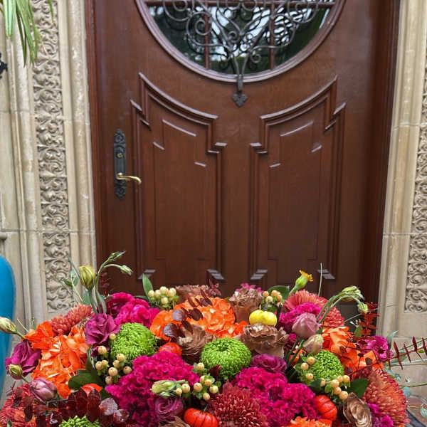 Large autumn floral arrangement in a magenta vase with orange, pink, and green blooms
