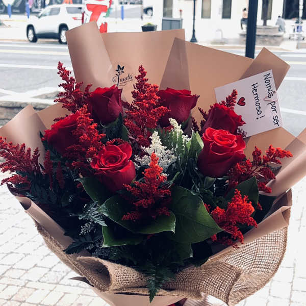 Bouquet of red roses with red filler flowers wrapped in tan paper