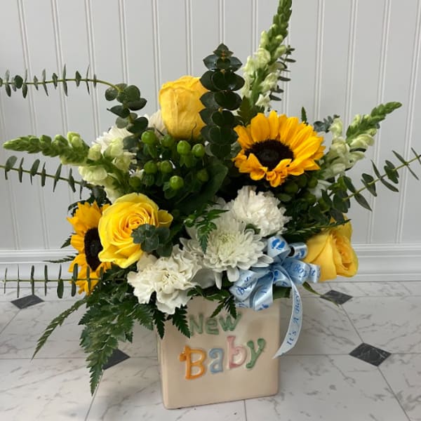 Yellow roses and sunflowers in a baby-themed container with a blue ribbon.