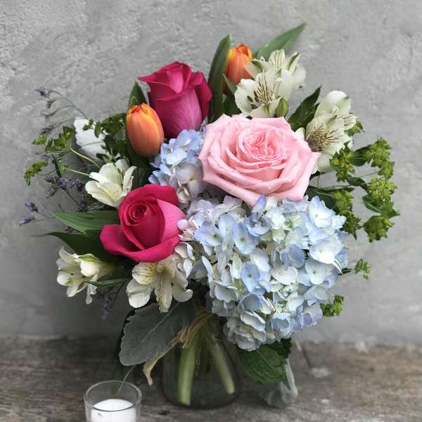 Bouquet of pink and orange roses with blue hydrangeas in a glass vase