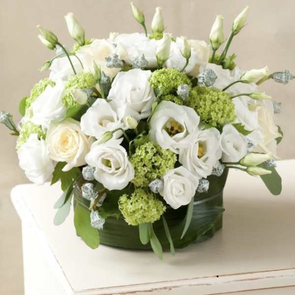 White roses and lisianthus arranged in a low round box