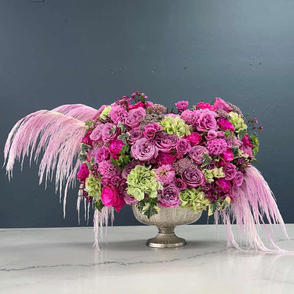 Pink and lavender floral arrangement in a silver urn with long pink feathers