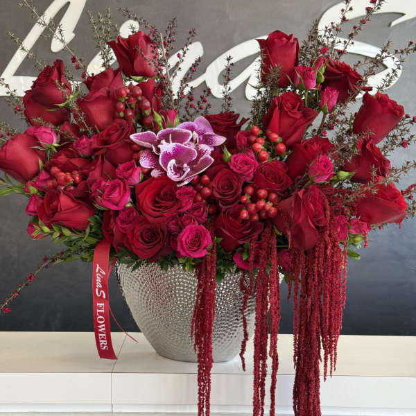 Red rose arrangement in a silver vase with trailing burgundy accents