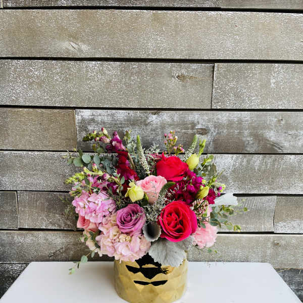 Mixed pink and red flower arrangement in a gold vase