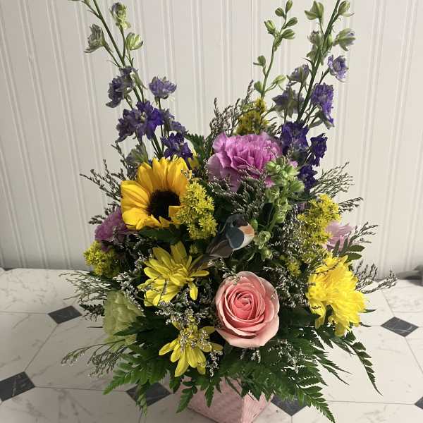 Mixed bouquet with pink rose, sunflower, purple blooms, and yellow daisies in a pink box