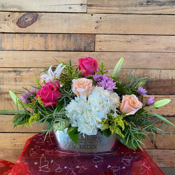 Low mixed arrangement of pink and peach roses, lilies, white hydrangea and purple mums in a metal tin container