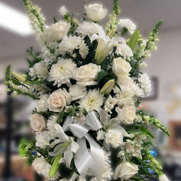 Tall white standing spray with roses, lilies, mums, and snapdragons on a stand with a white bow.