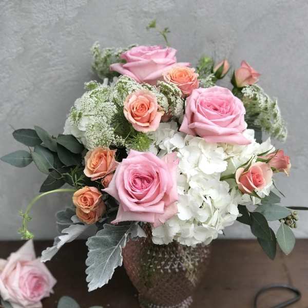 Pink and peach roses arranged with white hydrangea in a glass vase