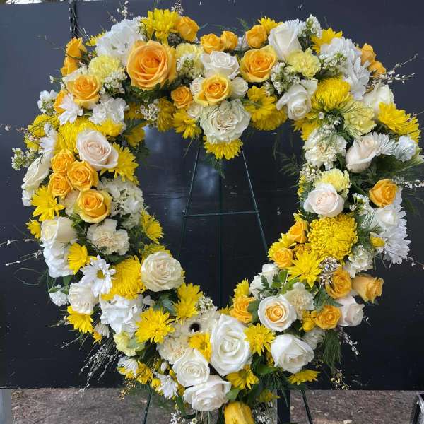 Heart-shaped floral wreath with yellow and white roses and daisies on an easel