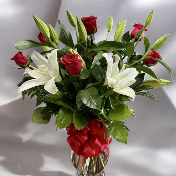 Red roses and white lilies arranged in a clear glass vase with a red ribbon.