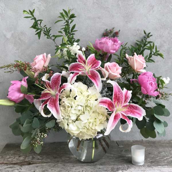 Pink lilies and roses arranged with white hydrangea in a glass vase