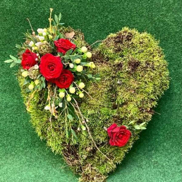 Heart-shaped moss arrangement with red roses and small white flowers