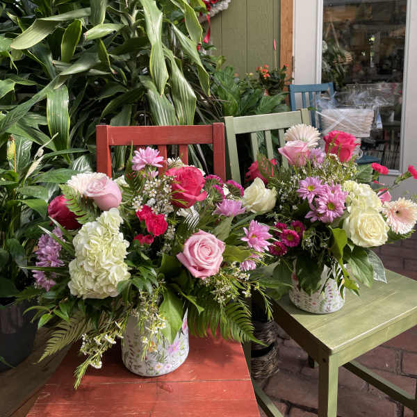 Two mixed flower arrangements in patterned containers on colorful chairs.