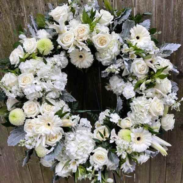 White floral wreath on a stand with roses and daisies