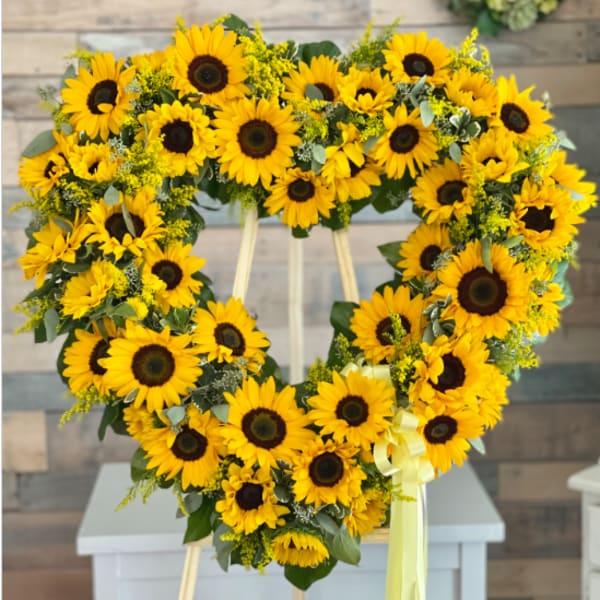 Heart-shaped sunflower wreath on a stand with a yellow ribbon