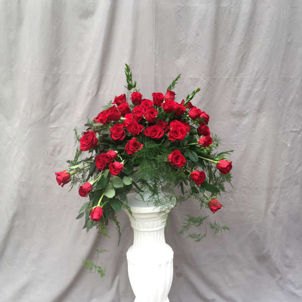 Red roses arranged in a tall white pedestal vase