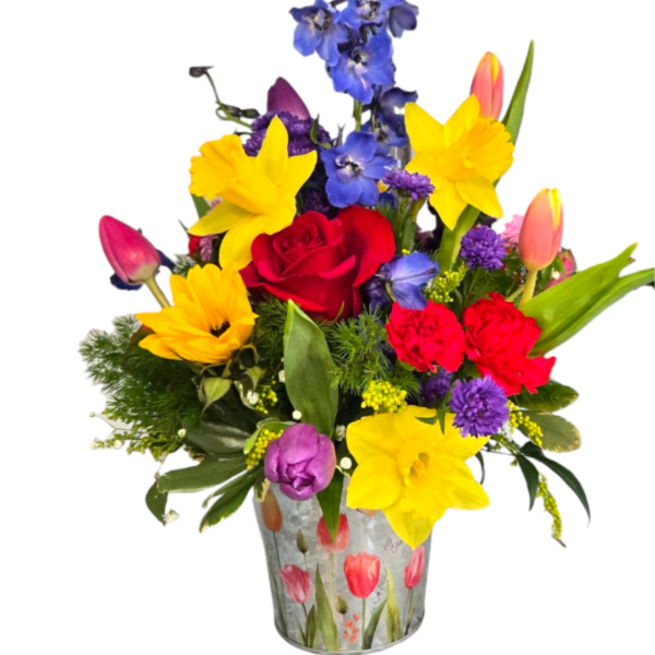 Colorful arrangement of yellow daffodils, red roses, tulips and blue delphinium in a printed metal bucket.