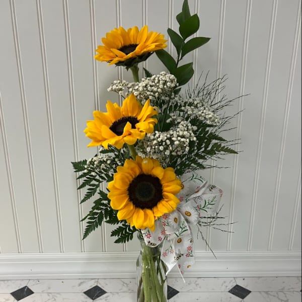 Tall sunflower arrangement in a clear glass vase with a patterned ribbon