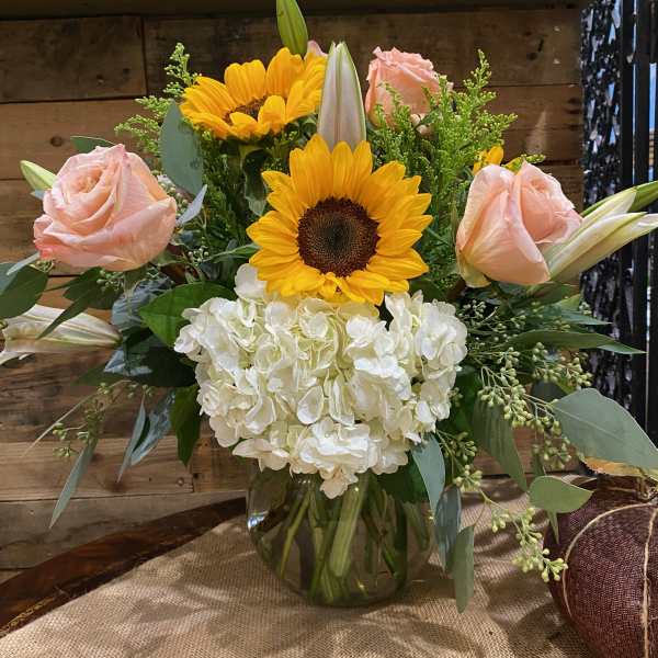 Sunflowers, pale pink roses, and white hydrangea in a glass vase