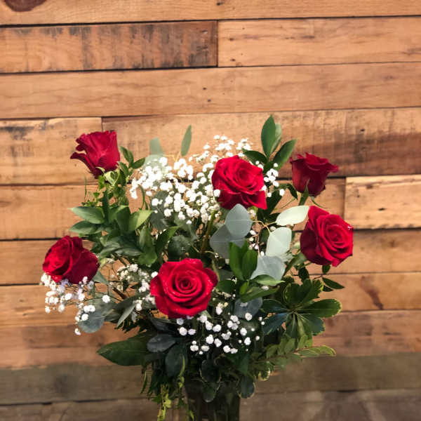 Red roses arranged in a clear glass vase with white baby's breath