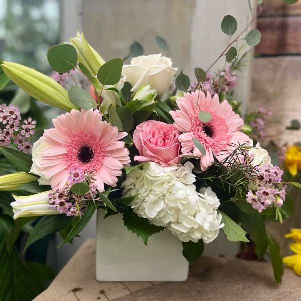 Pink gerbera daisies and roses in a white square vase
