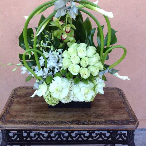 White floral arrangement with green loops and gray ribbon on a black base