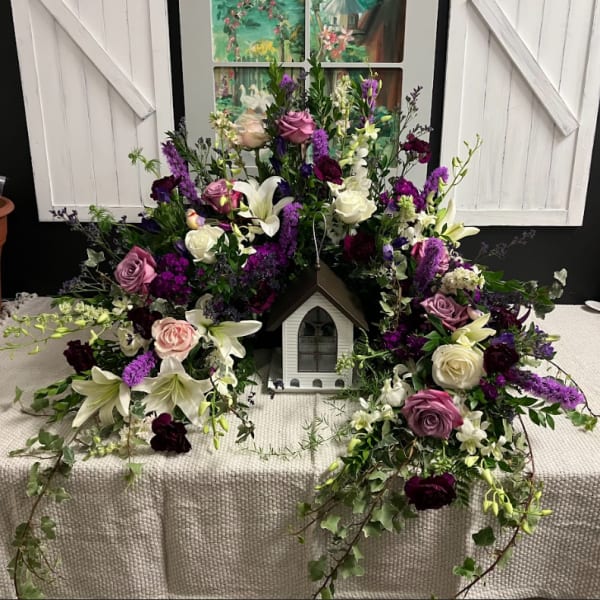 Floral wreath around a small decorative house with white and purple flowers