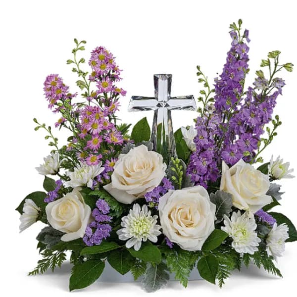 White roses and purple flowers arranged around a clear glass cross.