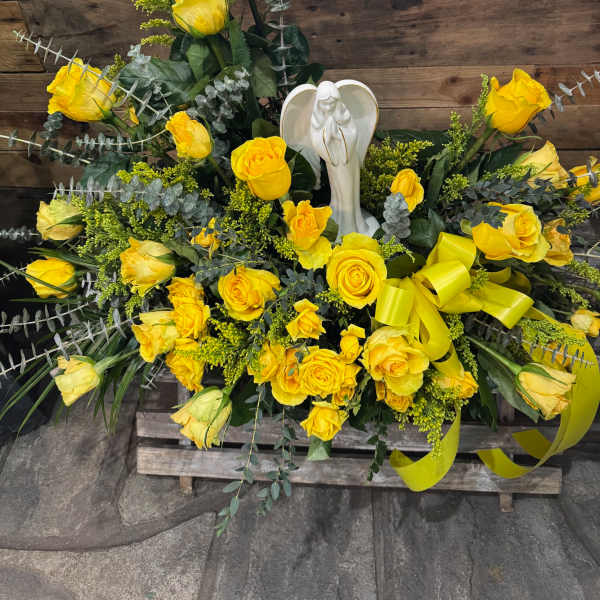Yellow rose funeral spray with an angel figurine and ribbon