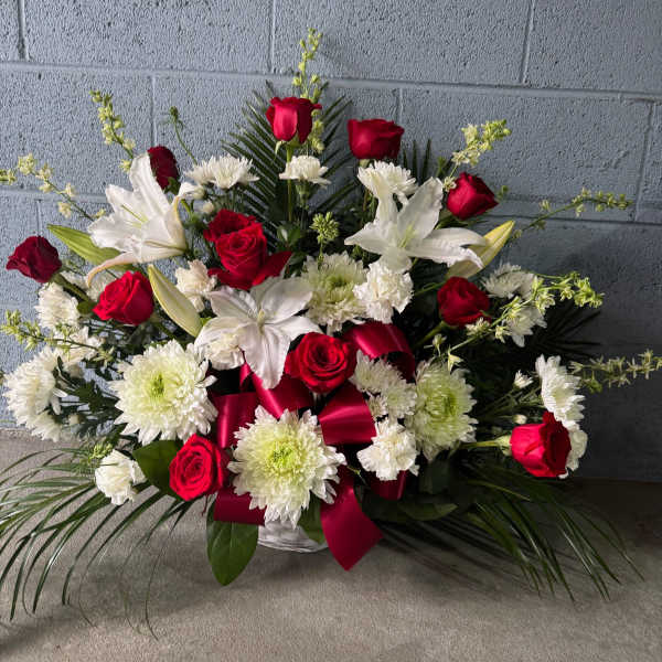 Red roses and white lilies in a low basket arrangement with a red ribbon