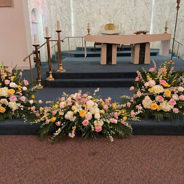 Three pastel floral arrangements on a church altar platform