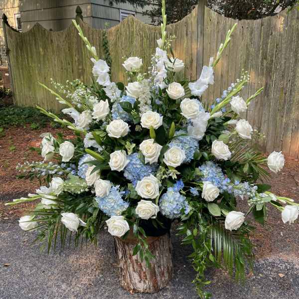 Large white and blue floral arrangement with roses and tall spikes in a wood base